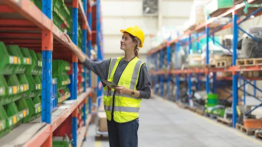 Warehouse operative in a hi-vis vest and hard hat checking stock on industrial racking